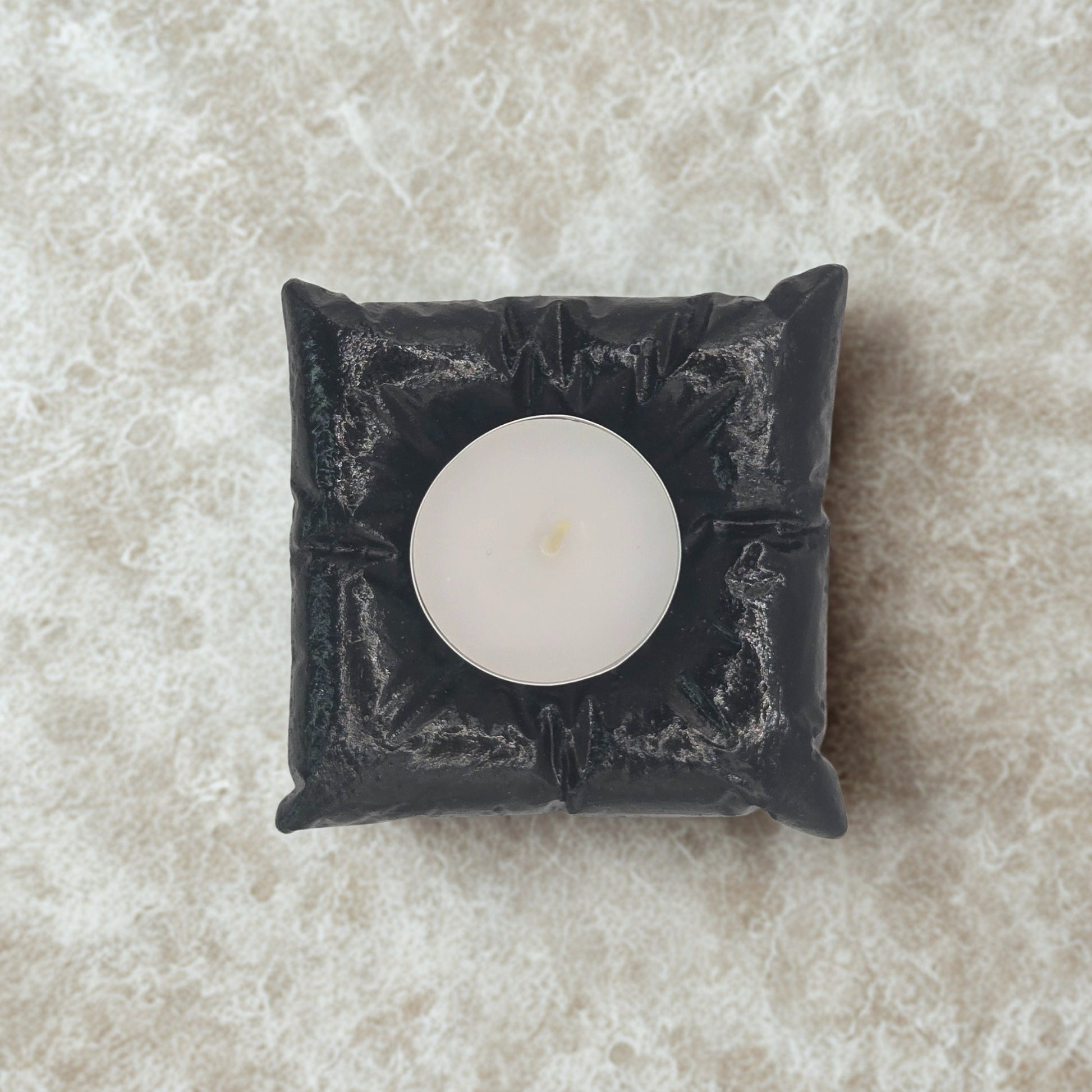 Black decorative candle holder with a white candle on a beige marble surface