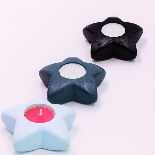 Star-shaped candle holders in black, blue, and light blue with candles inside on a white background.