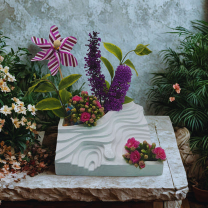 Decorative planter with flowers and a windmill on a stone surface with a garden background