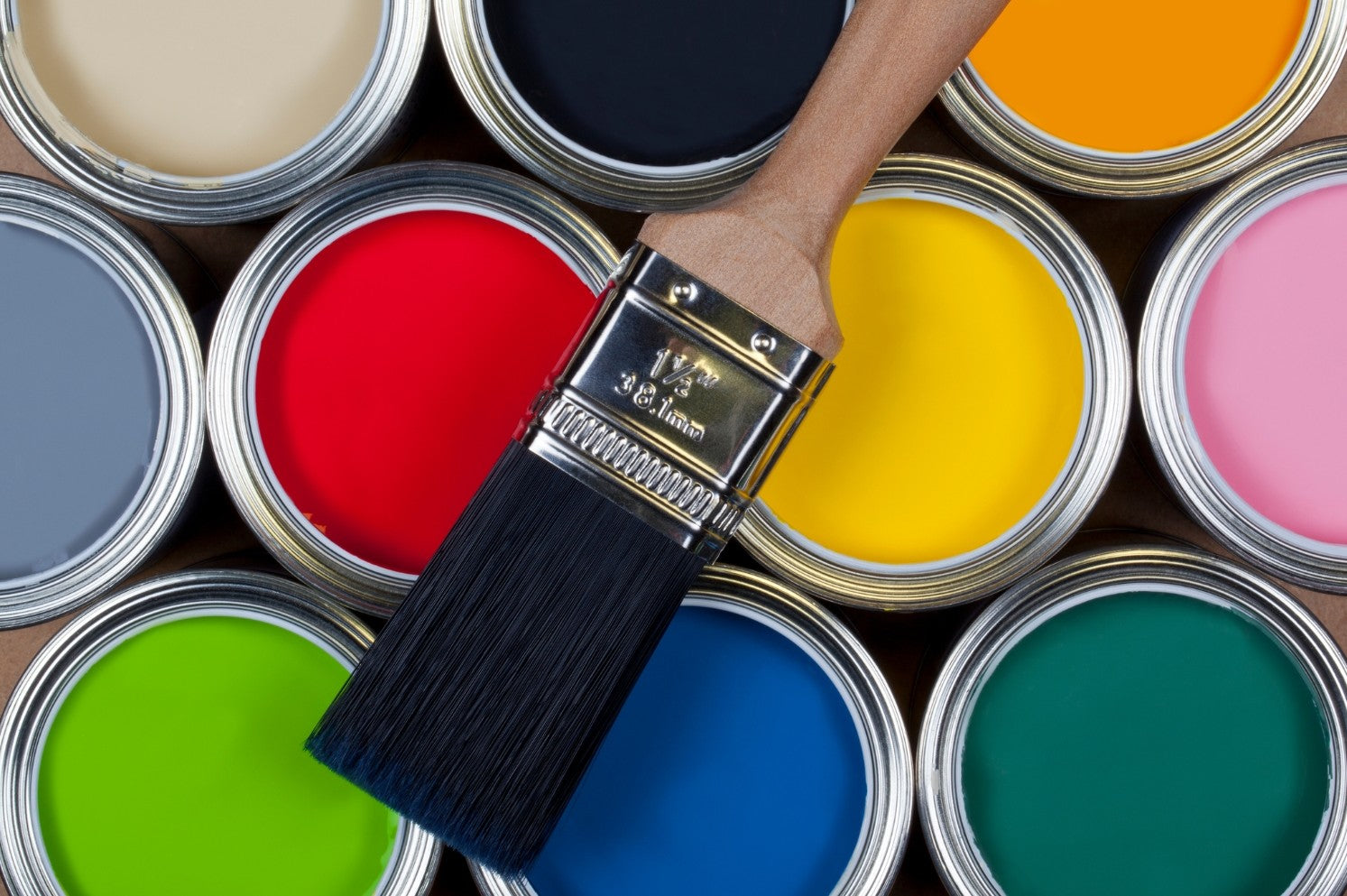 A paintbrush on top of tins of paint showing different colours
